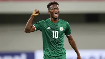 Temi Babalola, a young and energetic forward, celebrates his goal with a powerful fist pump and a wide grin, his number...
