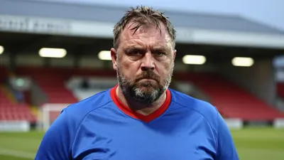A close-up shot of a middle-aged, stocky Hartlepool United coach, with a thick beard and a stern expression, his face...