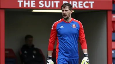 A 35-year-old male goalkeeper, built with a strong athletic build, stands in the low-lit tunnel at The Suit Direct...